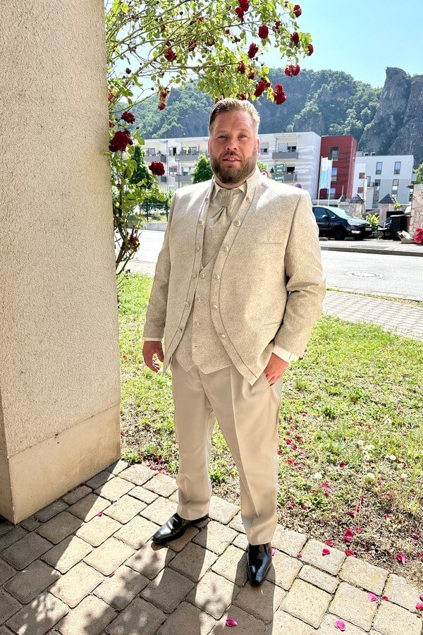 Herrenmode in Übergröße bei Biancas Brautmoden entdecken. Bräutigam in großer Größe trägt eleganten Tziacco-Gehrock mit Stehkragen, gemusterter Jacke und Plastron – Hochzeitsanzug in Beige bei Biancas Brautmoden
