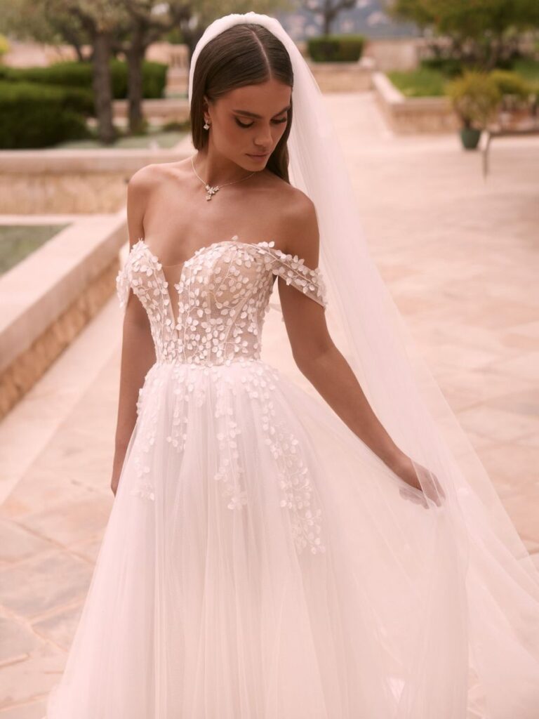 Romantisches Brautkleid mit schulterfreiem Oberteil, 3D-Blütenapplikationen und fließendem Tüllrock – Bianca’s Brautmoden in Bad Kreuznach.