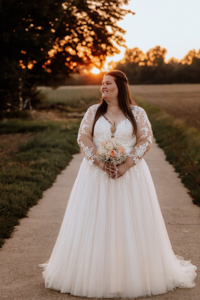 Curvy Braut im romantischen Spitzenkleid mit langen Ärmeln von Tres Chic – Bianca’s Brautmoden Plus-Size Brautkleider.