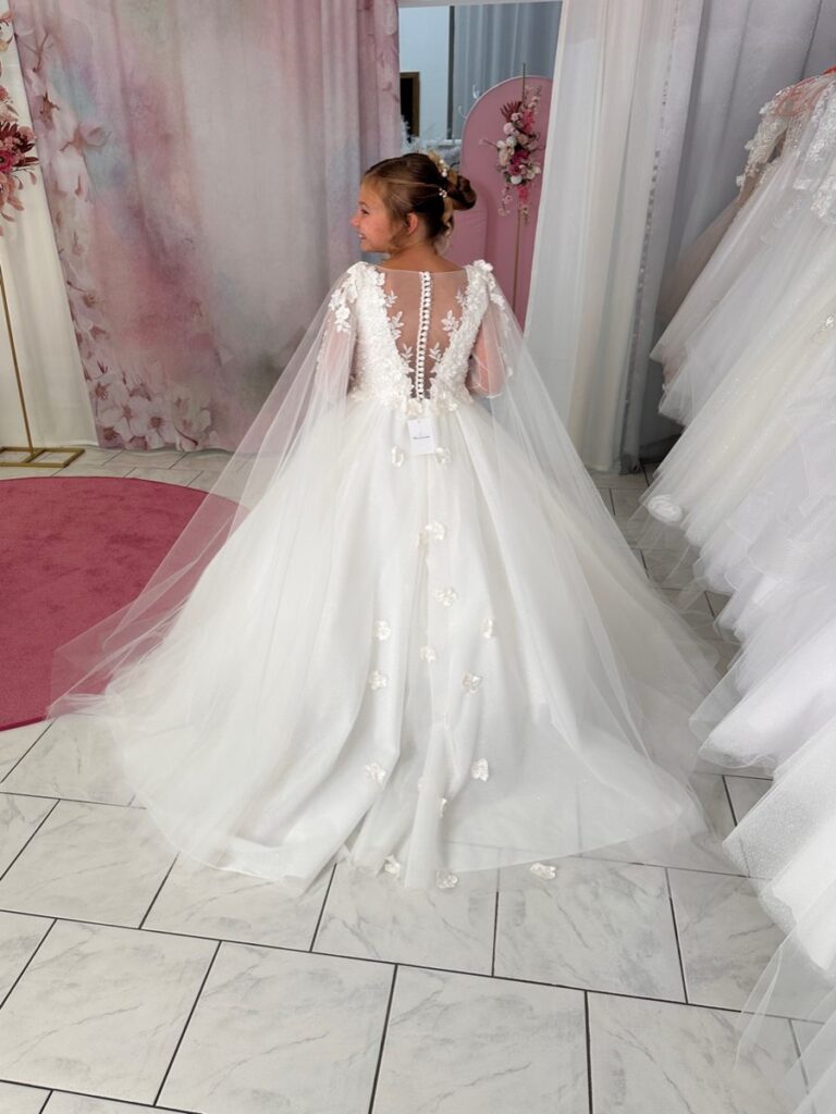 Kommunion 8 Kommunionkleid mit abnehmbarer Schleppe, Glitzertüll und 3D-Blüten – elegantes Modell mit Spitzenrücken für Kommunion 2026, erhältlich bei Bianca’s Brautmoden Bad Münster.