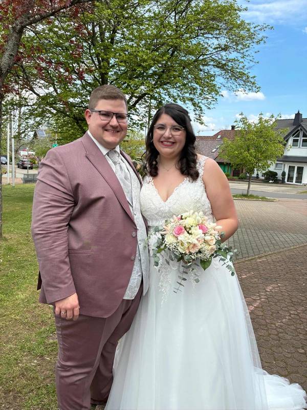 Echtes Brautpaar von Biancas Brautmoden. Er in einem bordeaux farbenen Anzug in großer Größe, sie in einem Brautkleid mit Trägern