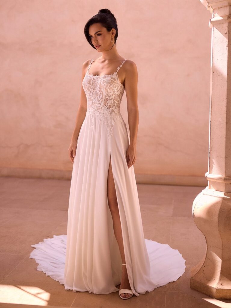 Fließendes A-Linien-Brautkleid mit Spitzenoberteil, schmalen Spaghettiträgern, Beinschlitz und langer Schleppe. Das moderne Hochzeitskleid verbindet romantische Spitze mit einem eleganten, schlichten Rock.