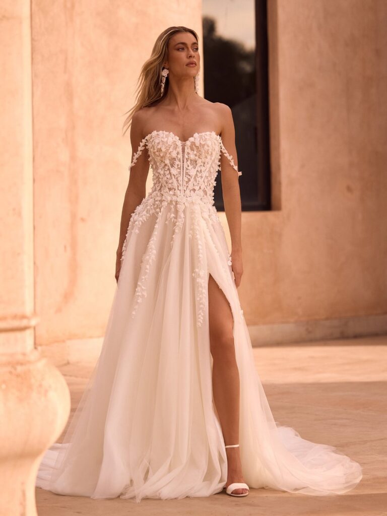 Romantisches A-Linien-Brautkleid mit floraler 3D-Spitze, Corsage in Stäbchenoptik, Off-Shoulder-Trägern und hohem Beinschlitz. Der fließende Tüllrock mit langer Schleppe verleiht dem Brautkleid einen modernen und eleganten Look.