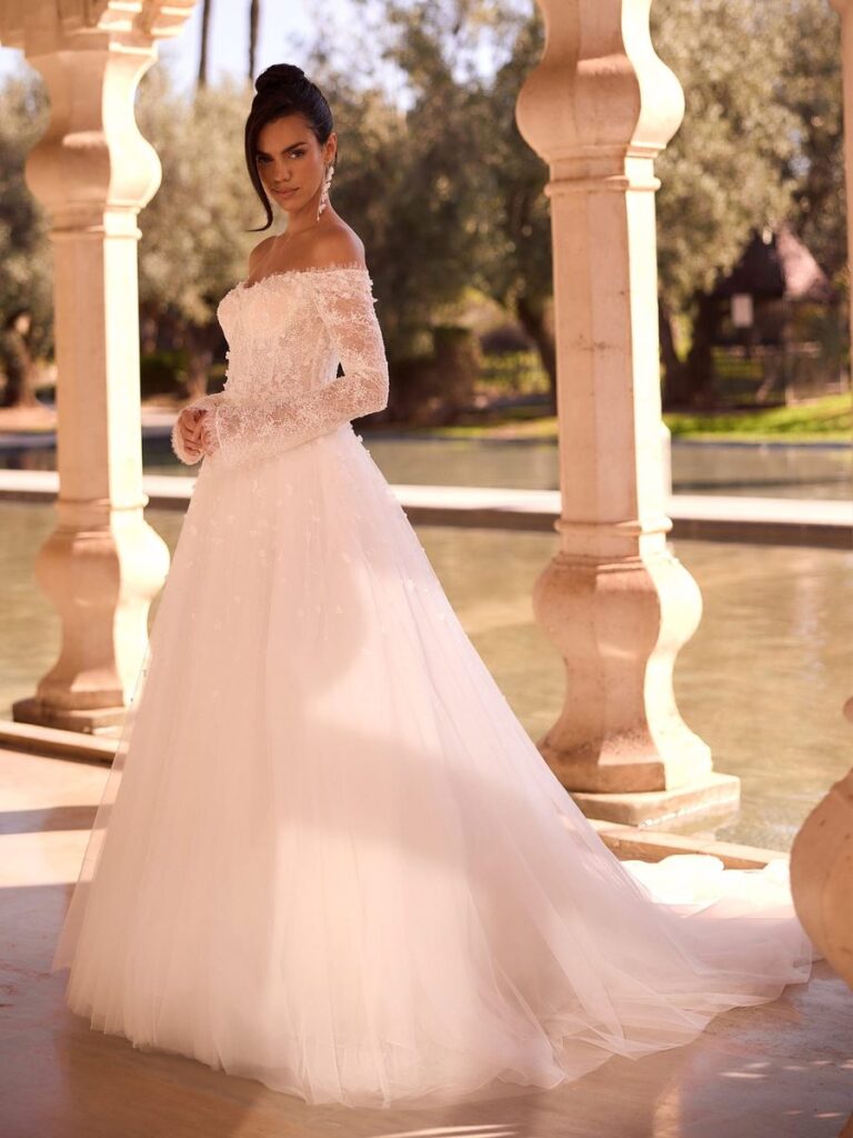 Romantisches A-Linien-Brautkleid mit Off-Shoulder-Ausschnitt, langen Spitzenärmeln und funkelndem Tüllrock. Das elegante Prinzessinnenbrautkleid vereint zeitlose Eleganz mit moderner Leichtigkeit und einer langen Schleppe.